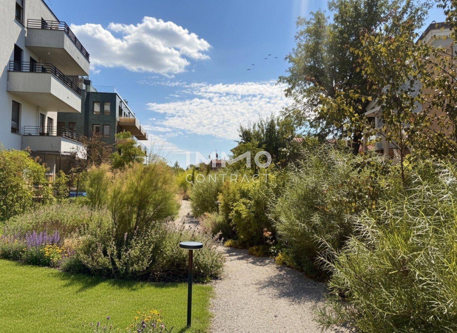 Gepflegter Gartenweg mit üppiger Bepflanzung und modernen Wohngebäuden im Hintergrund.