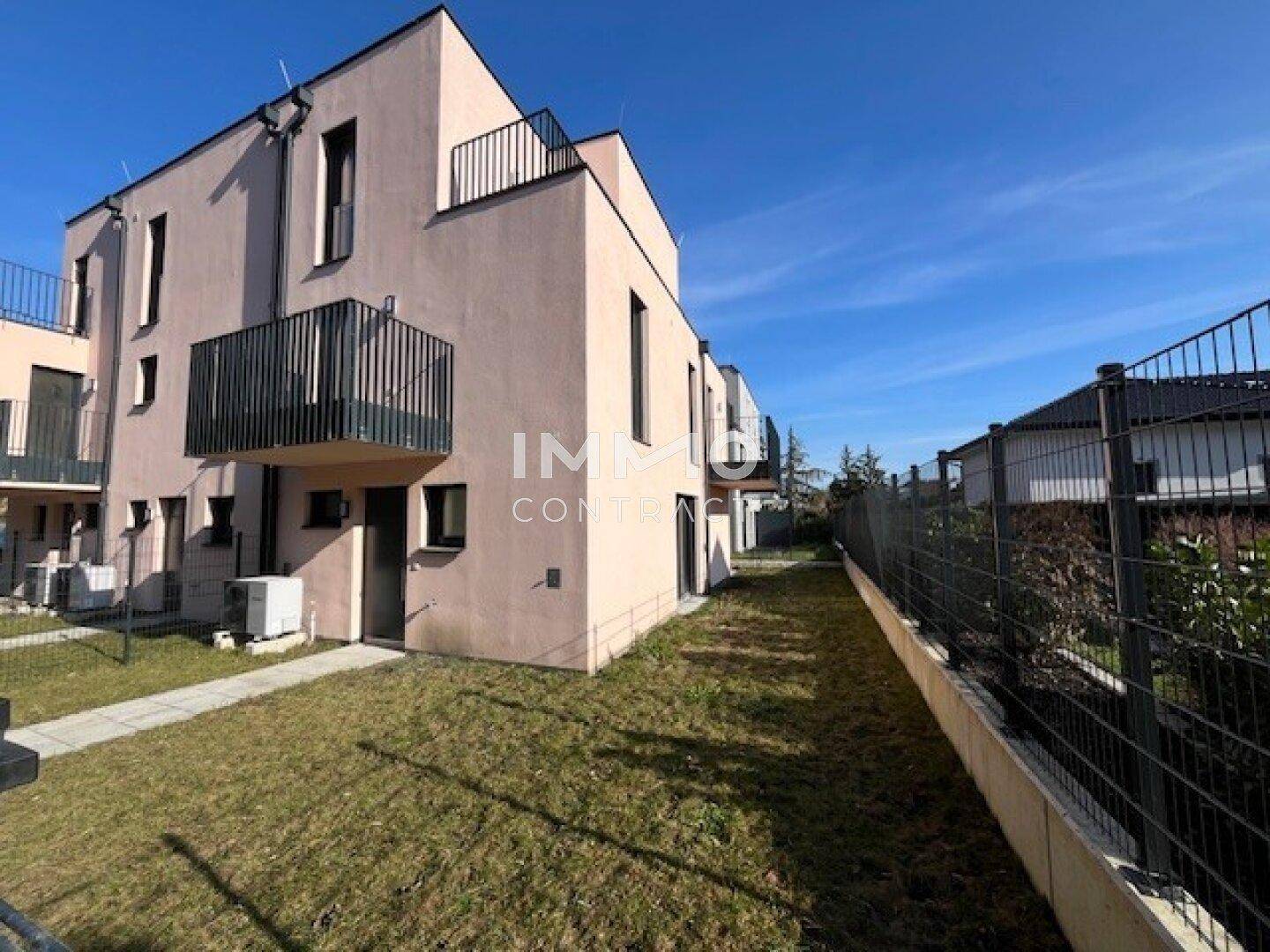 Rückseite eines modernen Reihenhauses mit Garten, Balkonen und Zaun.