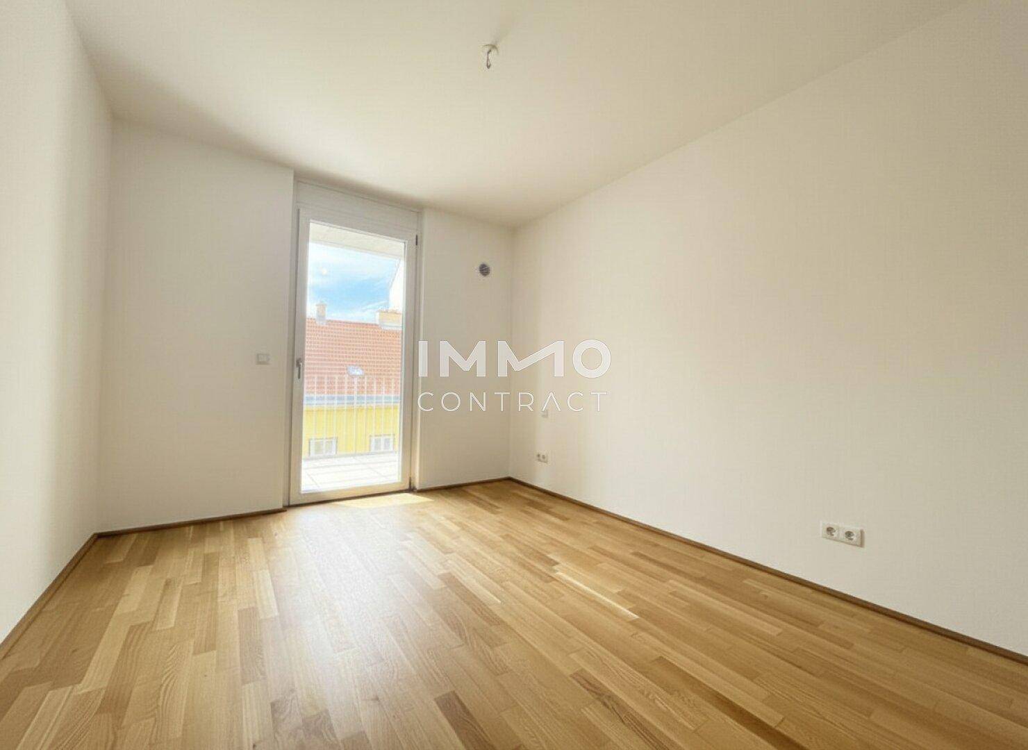 Leeres Schlafzimmer mit hellem Parkettboden und direktem Zugang zum Balkon.