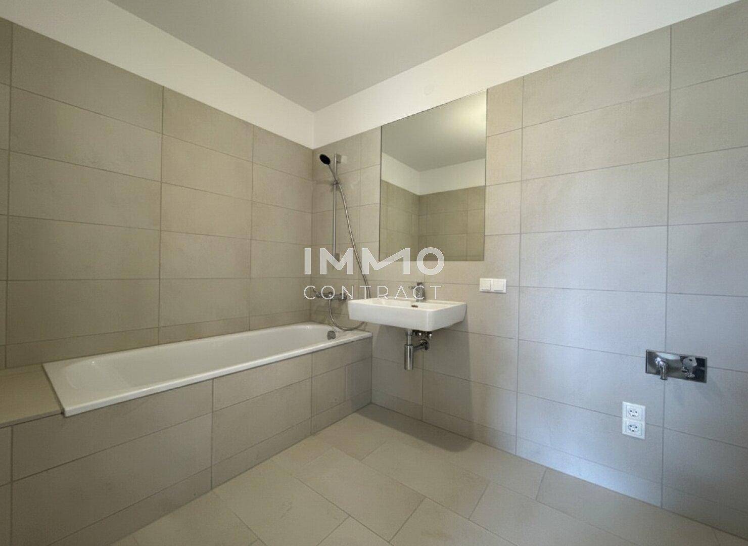 Modernes Badezimmer mit Badewanne, Waschbecken und großen hellgrauen Fliesen.