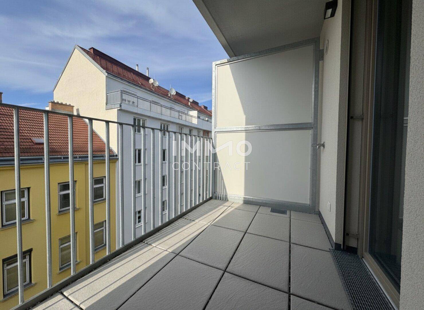 Kleiner Balkon mit Fliesenboden und Metallgeländer, Blick auf umliegende Gebäude.