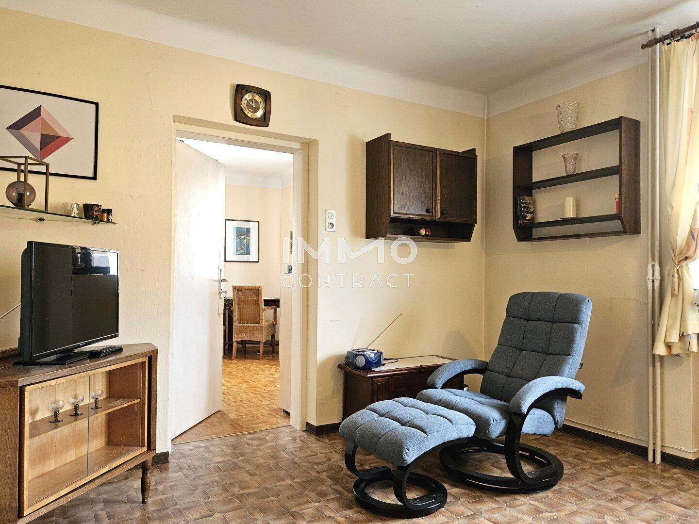 Wohnzimmer mit Sessel, Fernseher und Blick in einen angrenzenden Raum.