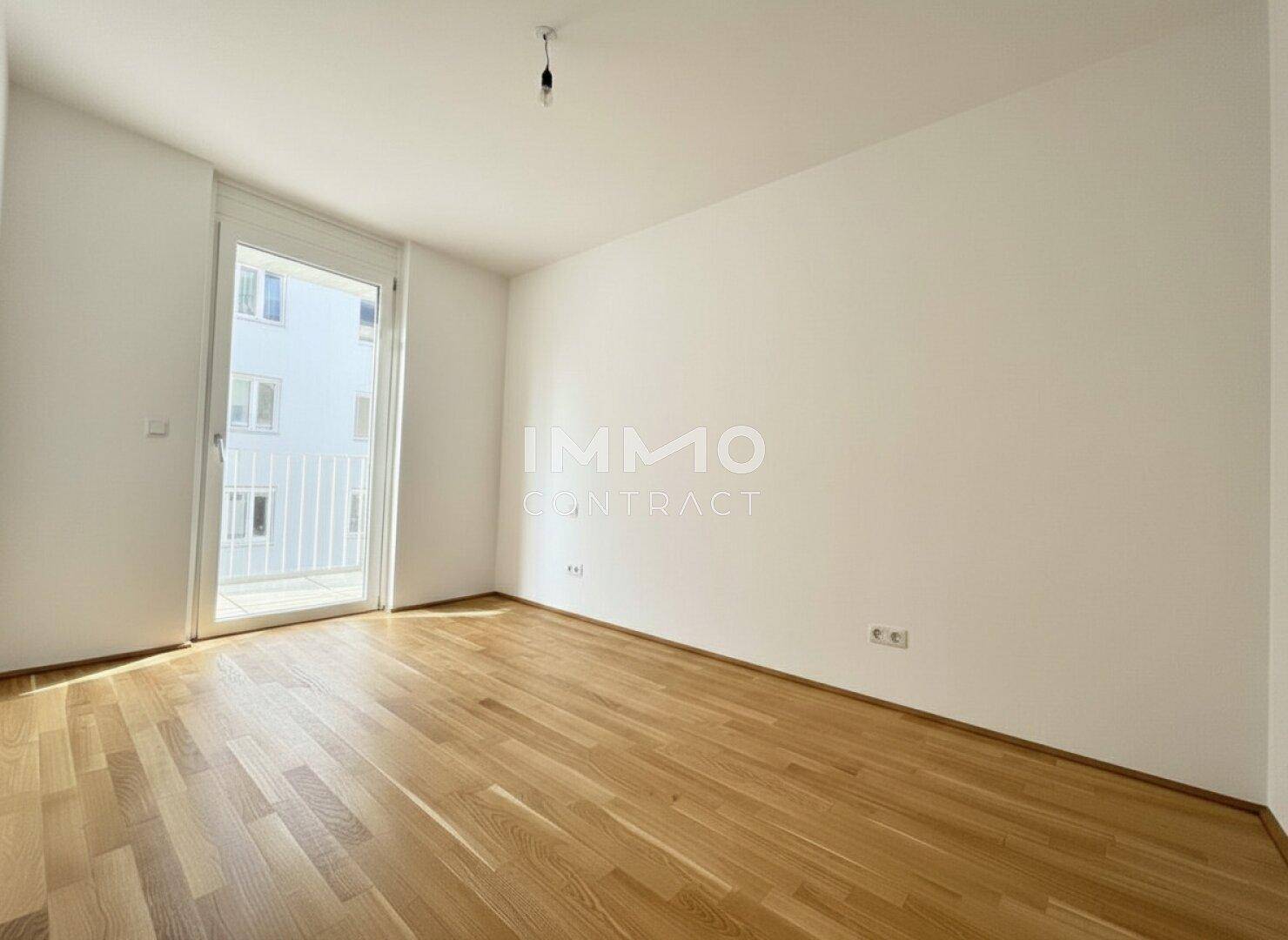 Helles, leeres Schlafzimmer mit Holzboden und Zugang zu einem französischen Balkon.