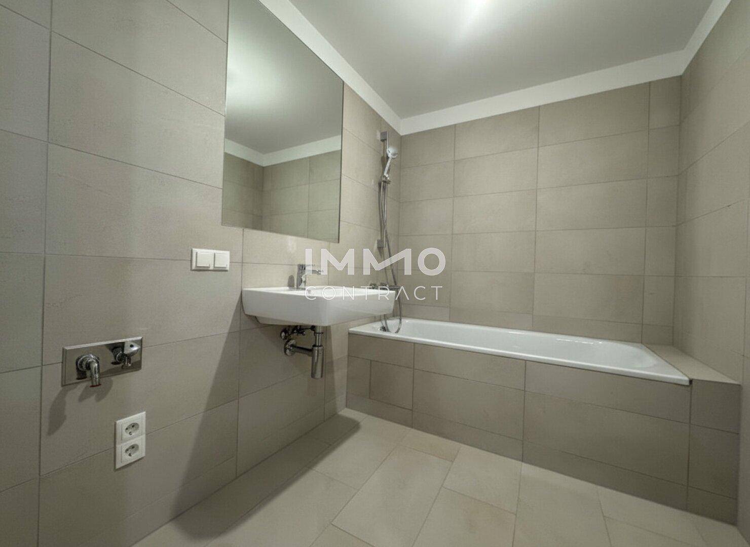 Modernes Badezimmer mit Badewanne, Waschbecken und großen grauen Fliesen.