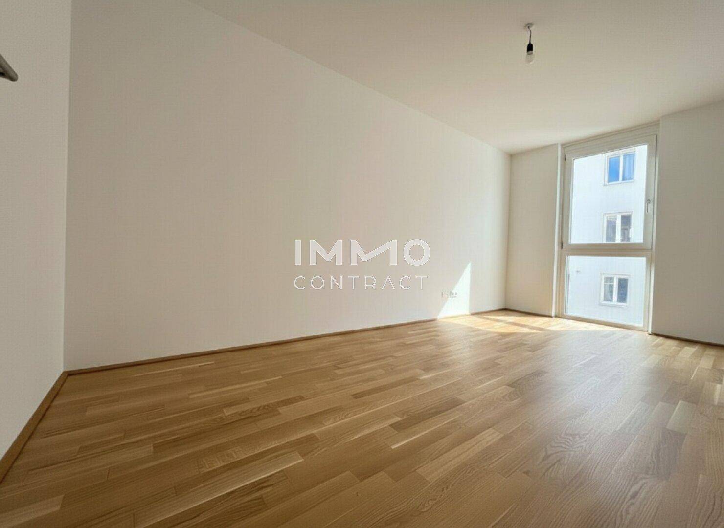 Helles, leeres Zimmer mit Holzboden und großem Fenster, ideal als Schlafzimmer oder Büro.