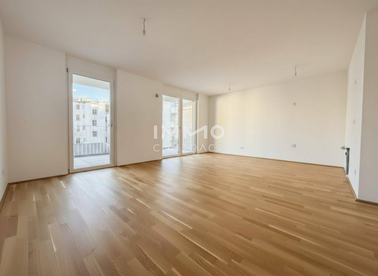 Geräumiges, leeres Wohnzimmer mit Holzboden und Zugang zu einem Balkon.