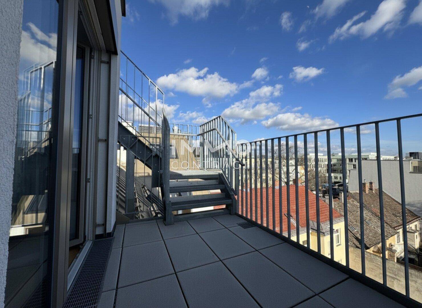 Geräumige Dachterrasse mit Metallgeländer und Treppe, die zu einer weiteren Ebene führt, mit Stadtblick.
