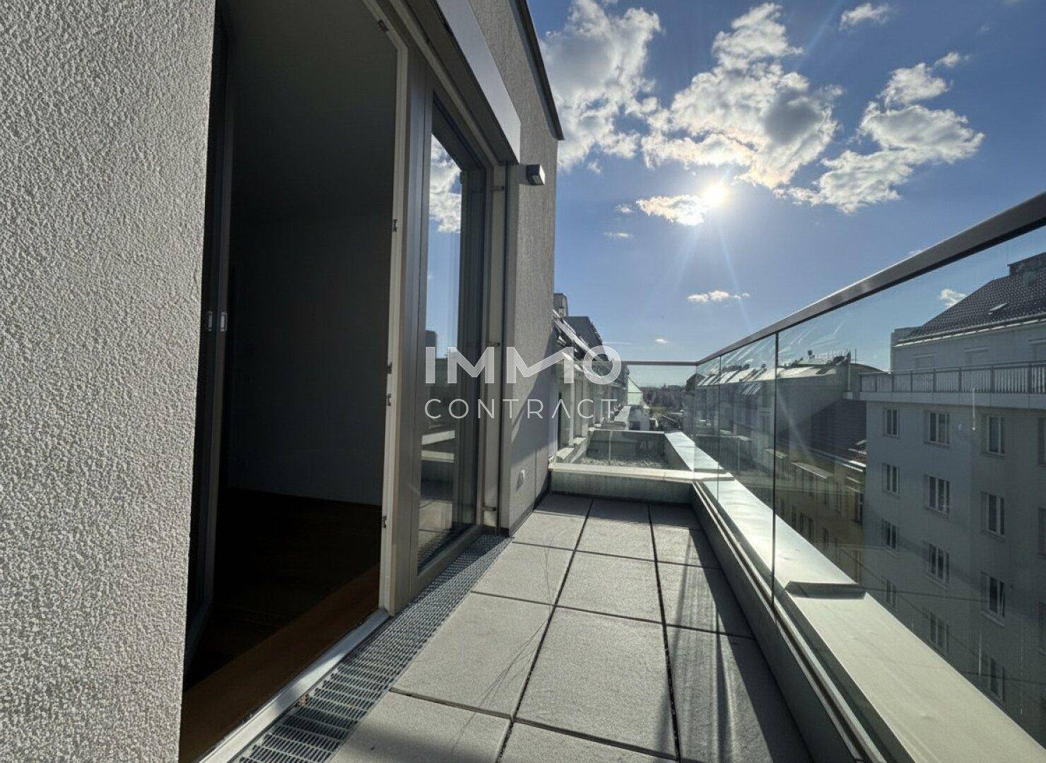 Moderner Balkon mit Glasgeländer und Schiebetür, der einen weiten Blick über die Stadt bietet.