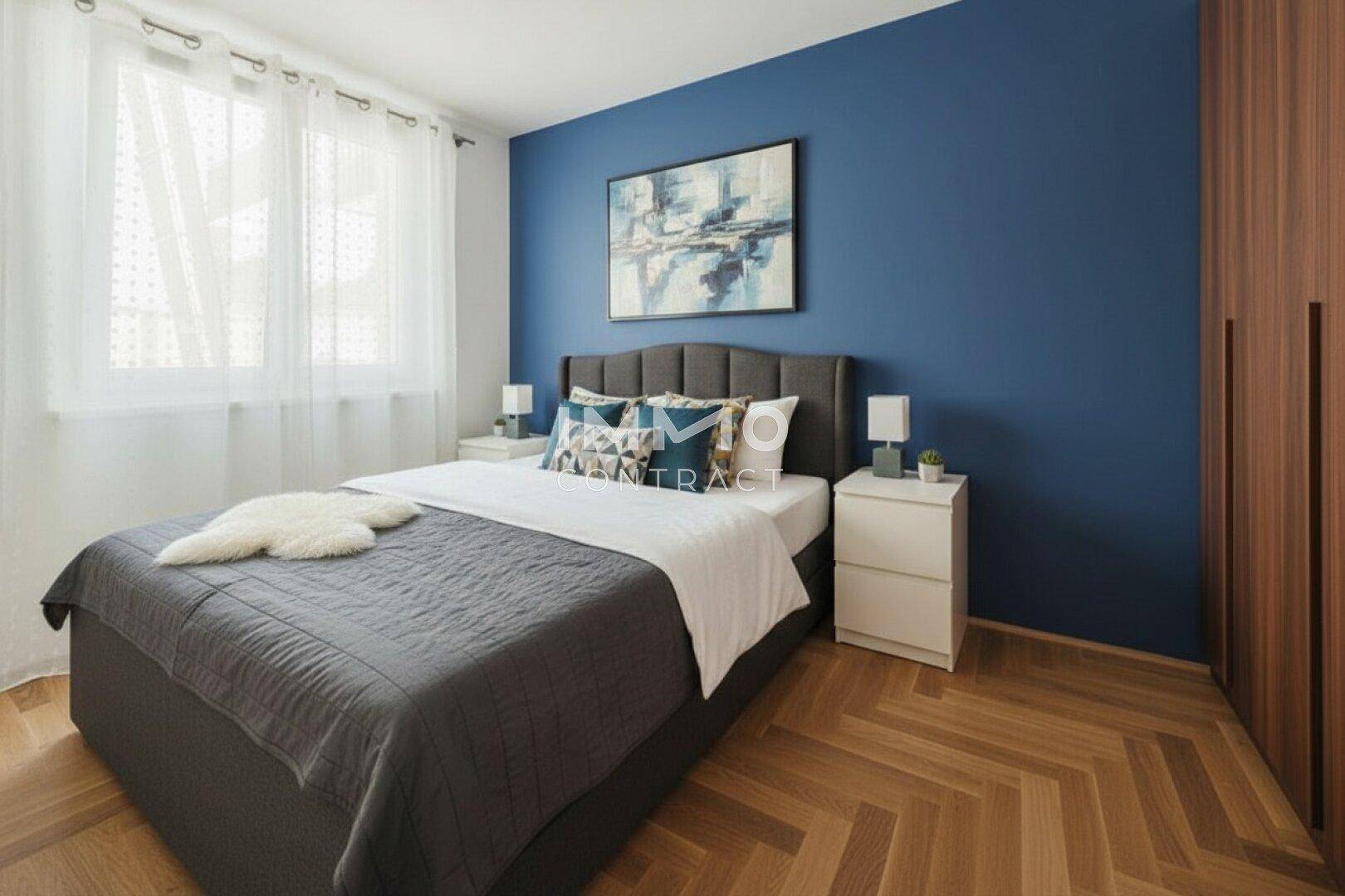 Gemütliches Schlafzimmer mit blauer Akzentwand, Parkettboden und großem Fenster.