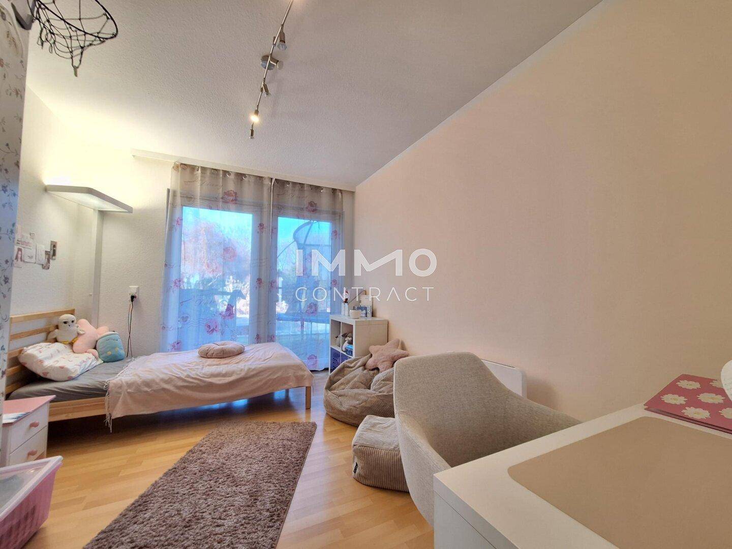 Helles Kinderzimmer mit Einzelbett, Schreibtisch und großen Fenstern zum Außenbereich.