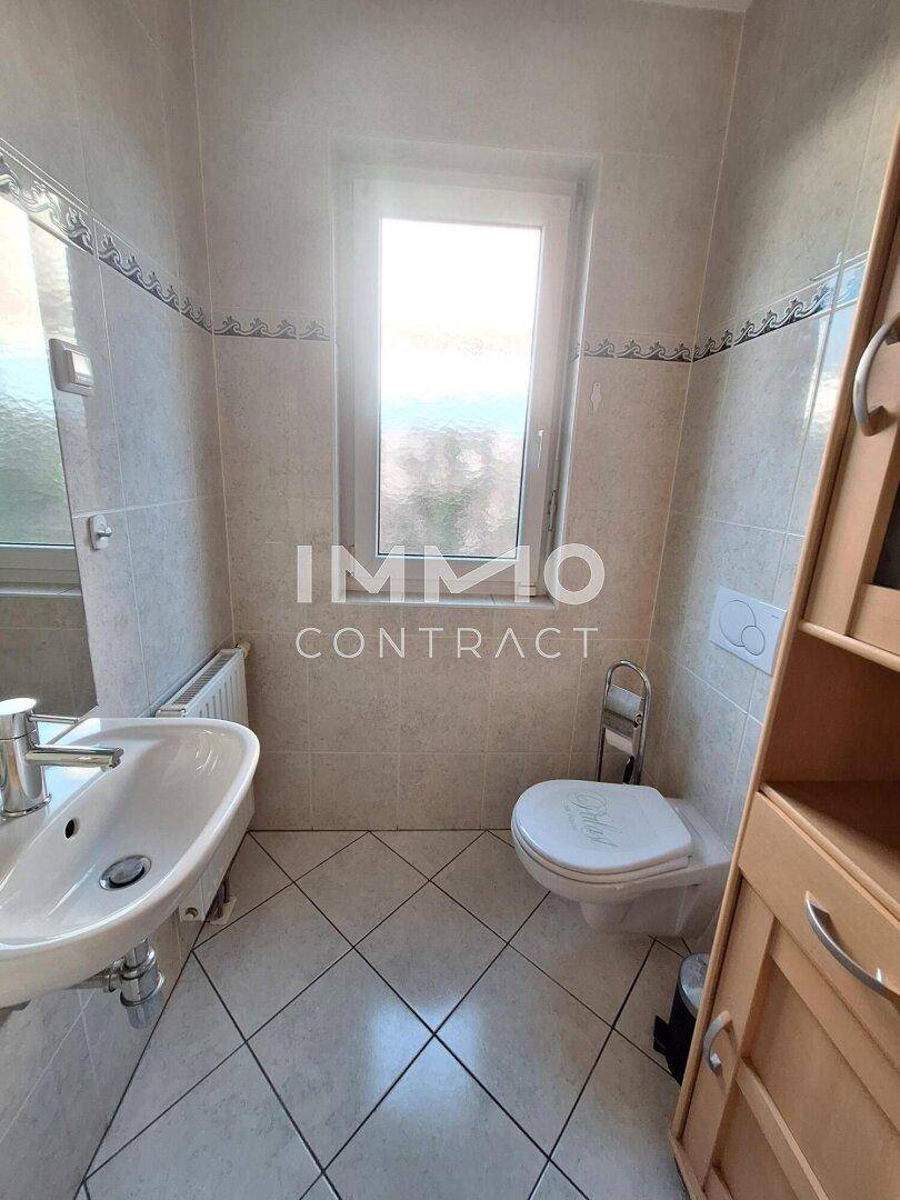 Helles Gäste-WC mit Fenster, Waschbecken und Wand-WC.