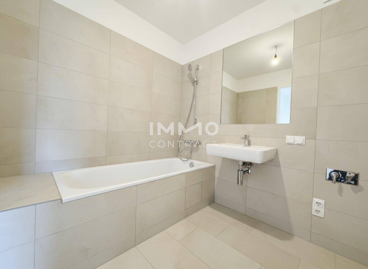 Modernes Badezimmer mit Badewanne, Einzelwaschbecken und großen Wandfliesen.