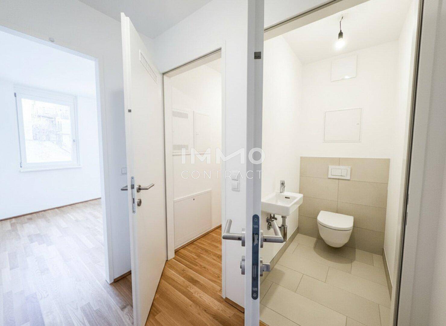 Helles Gäste-WC mit Wand-WC, kleinem Waschbecken und modernen Fliesen.