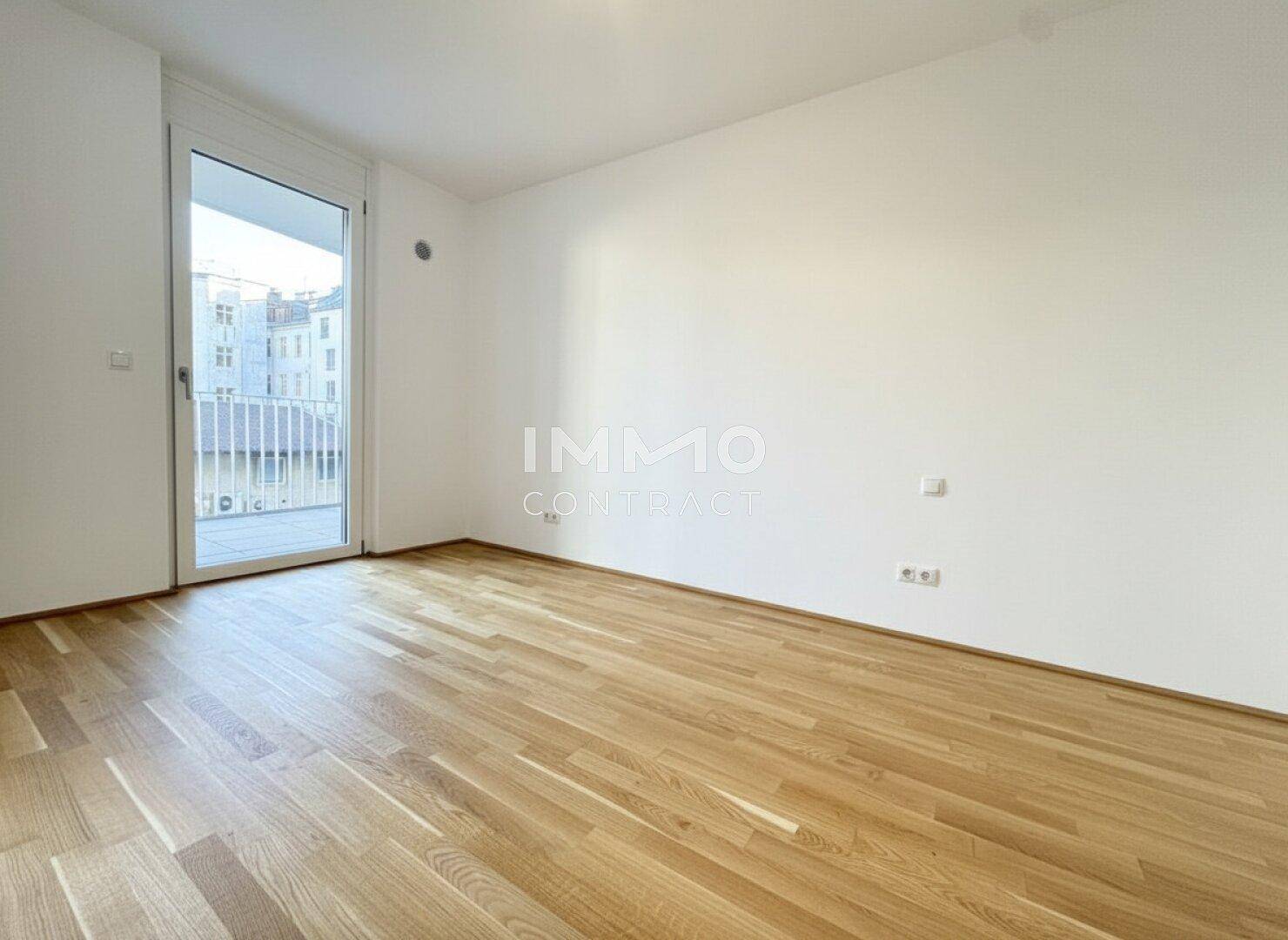Geräumiges Schlafzimmer mit Parkettboden, weißen Wänden und Zugang zum Balkon.