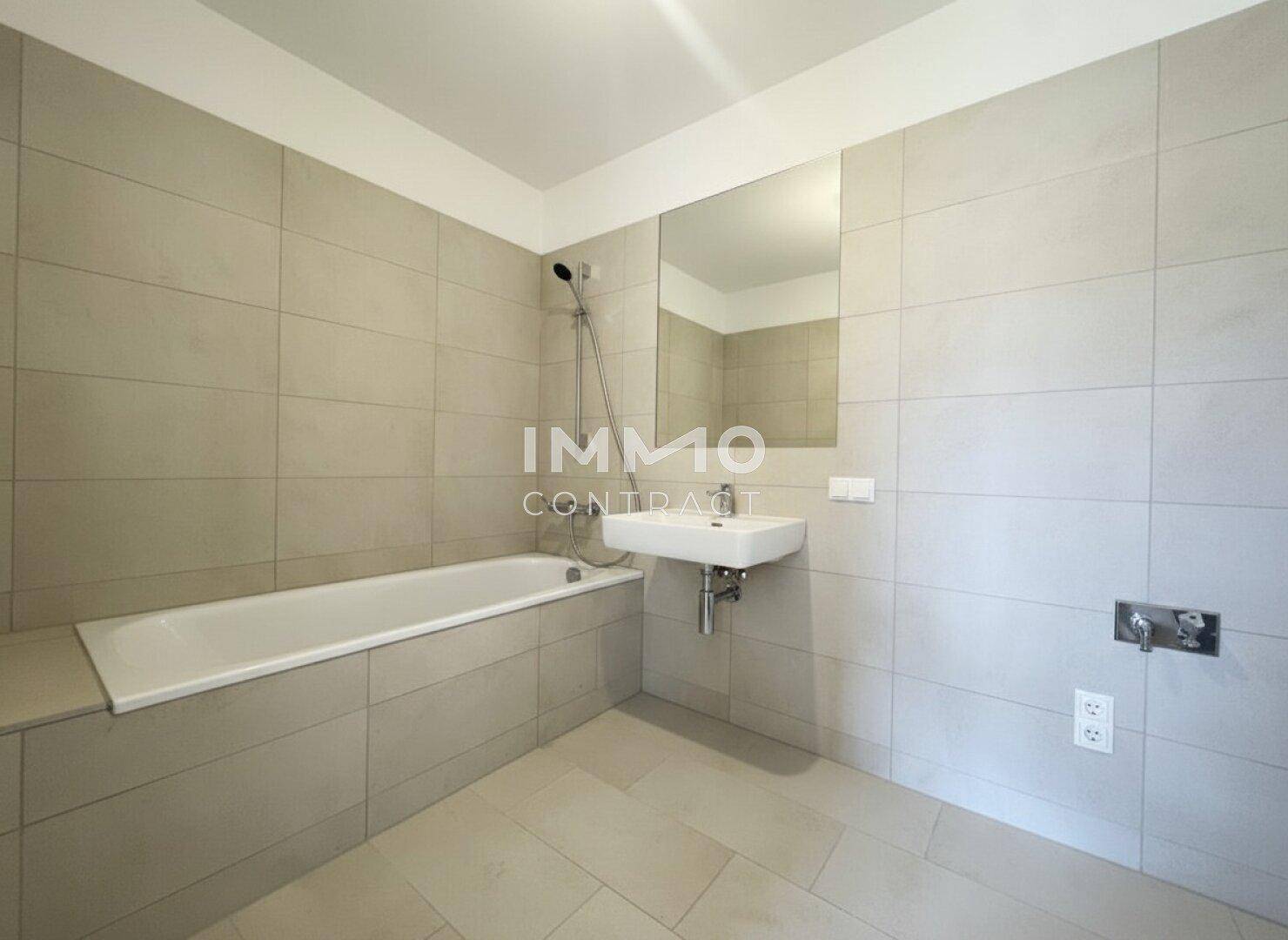 Modernes Badezimmer mit Badewanne, Waschbecken und hellen Fliesen an Wänden und Boden.