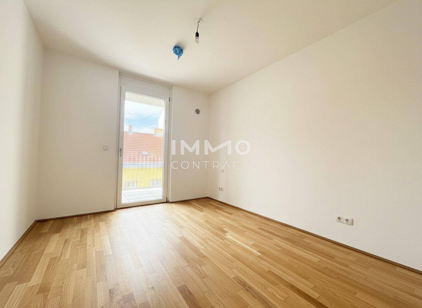 Leeres Schlafzimmer mit Holzboden und Zugang zu einem Balkon, hell und unmöbliert.