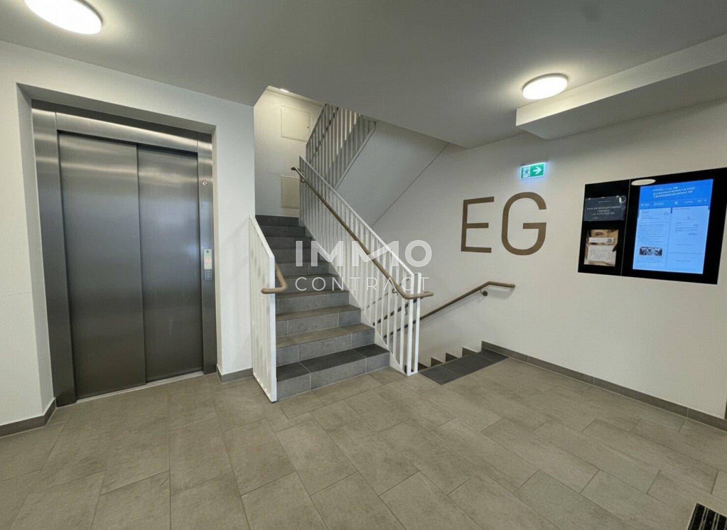 Eingangsbereich eines Mehrfamilienhauses mit Treppenhaus und modernem Aufzug aus Edelstahl.