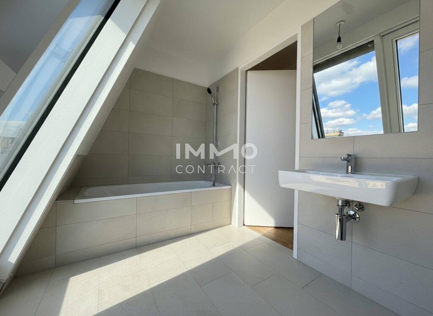 Helles Badezimmer mit Badewanne, modernem Waschbecken und großem Dachfenster.