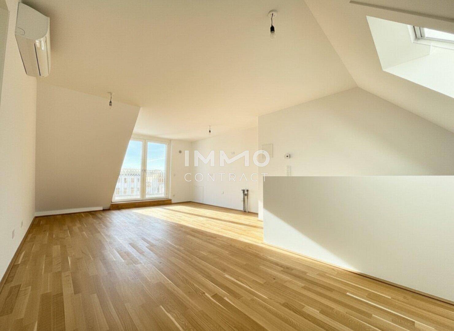 Heller Wohnraum mit Holzboden, großen Fenstern und Klimaanlage unter einer Dachschräge.