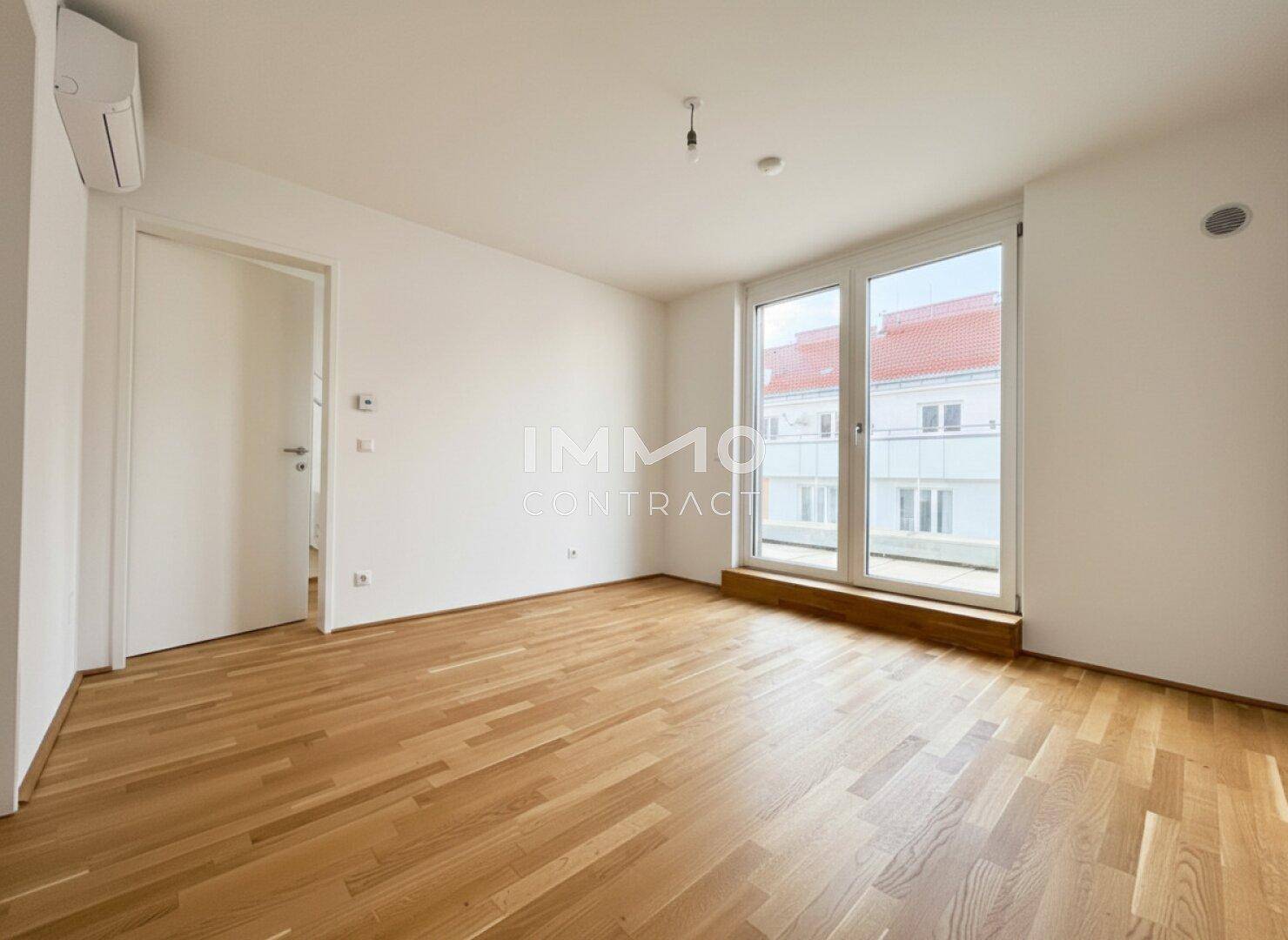 Geräumiger Wohnraum mit Parkettboden, großen Glasfenstern und Zugang zu einem Außenbereich.