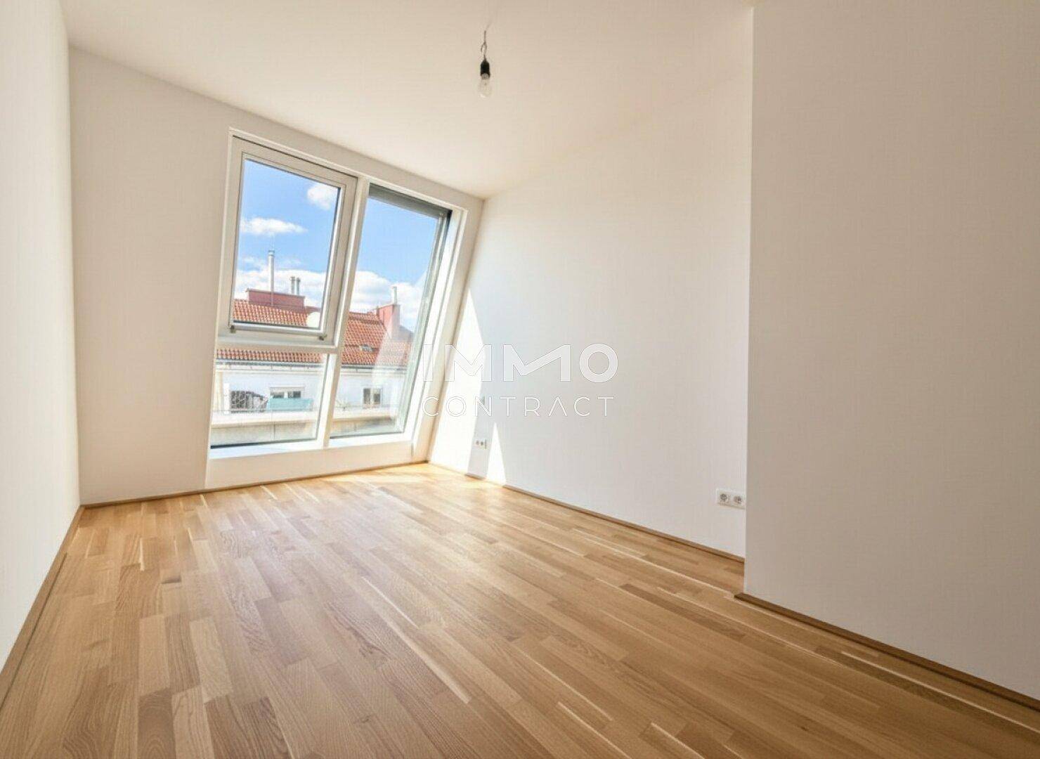 Helles Schlafzimmer mit Parkettboden und großem Fenster unter einer Dachschräge mit Blick auf Dächer.