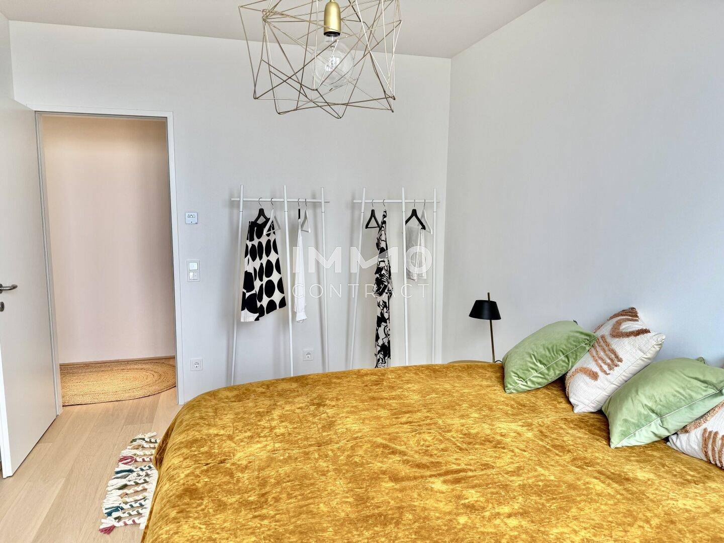 Helles Schlafzimmer mit Doppelbett, modernem Kleiderständer und hellem Holzfußboden.