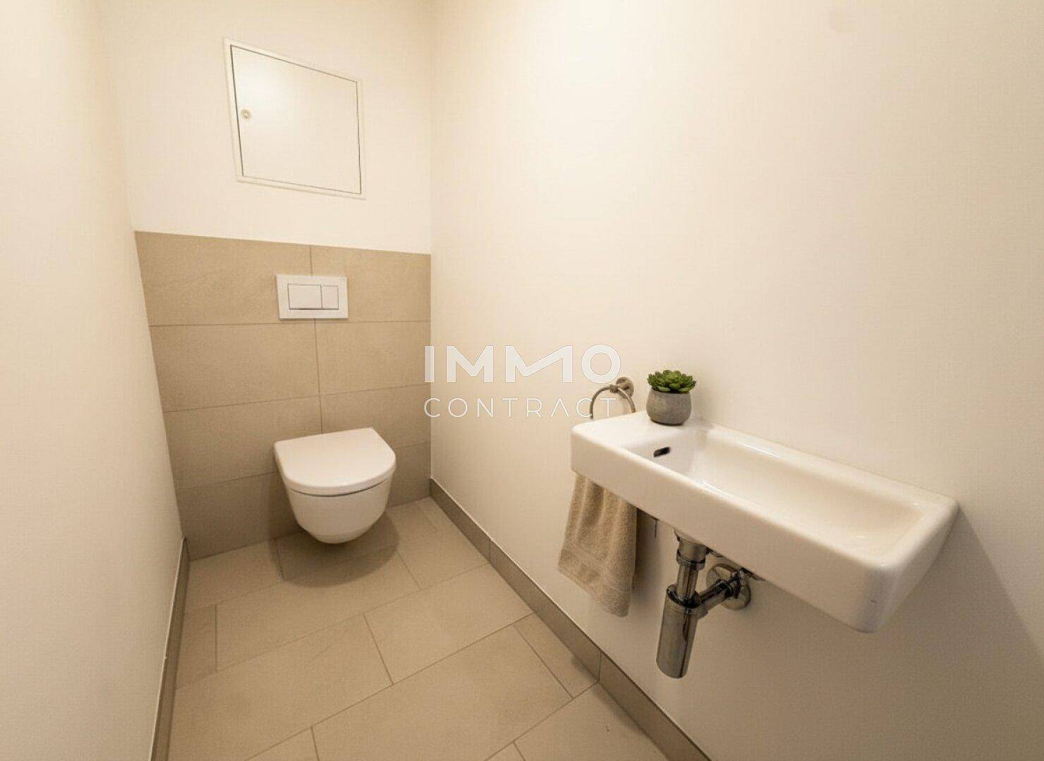 Kleines Gäste-WC mit Wand-WC, Waschbecken und hellen Fliesen.