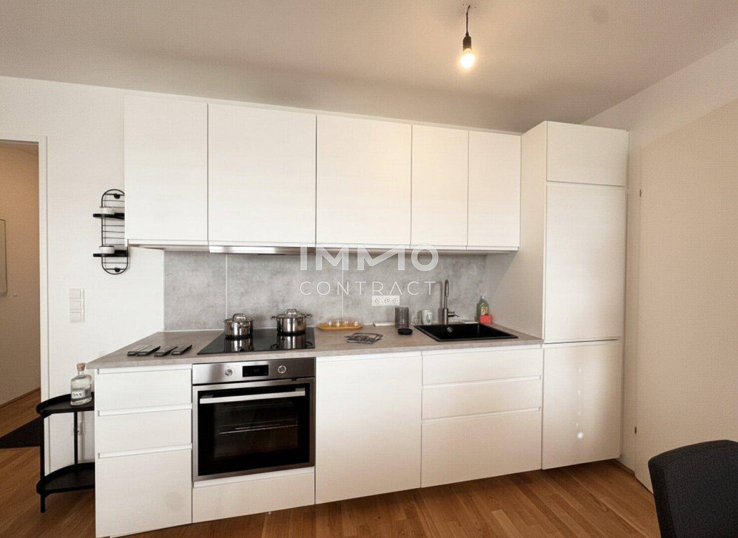 Moderne Einbauküche mit weißen Schränken, Induktionskochfeld und integriertem Backofen.