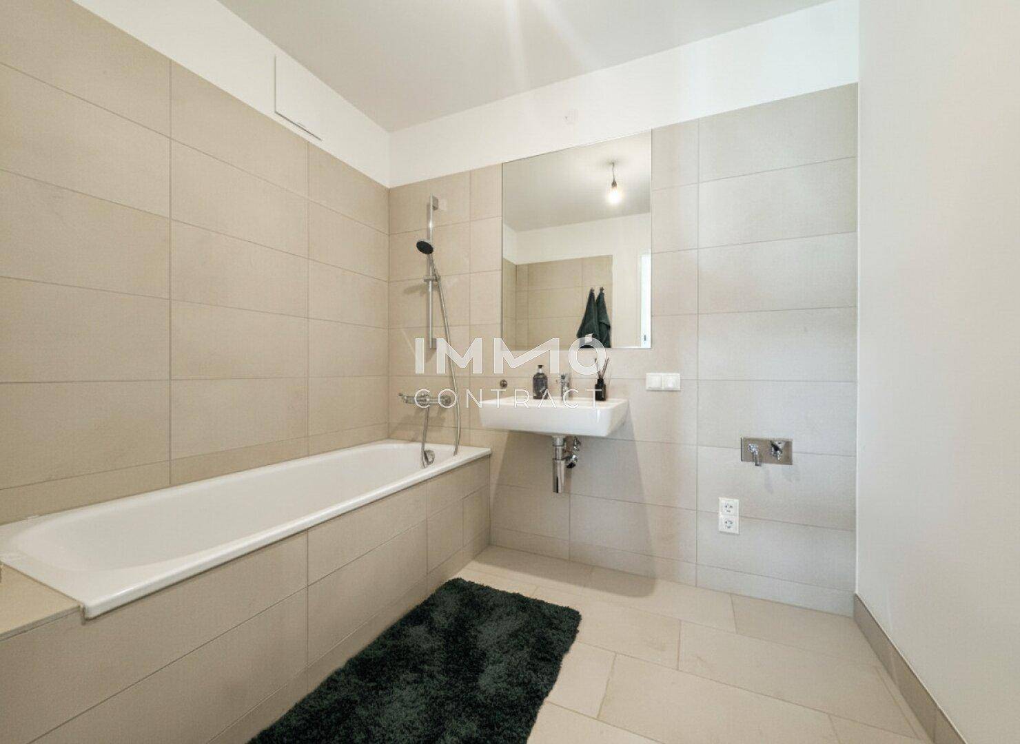 Modernes Badezimmer mit Badewanne, beigefarbenen Fliesen und schlichtem Design.