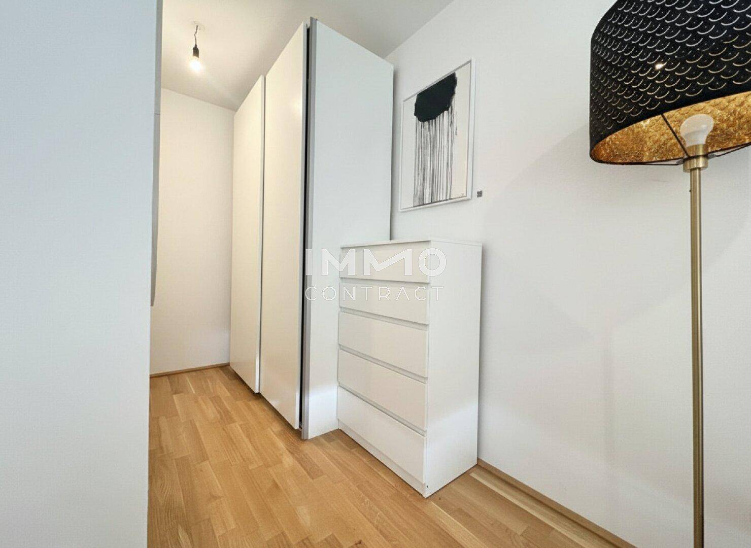 Heller Flur mit weißen Einbauschränken und Holzparkettboden.