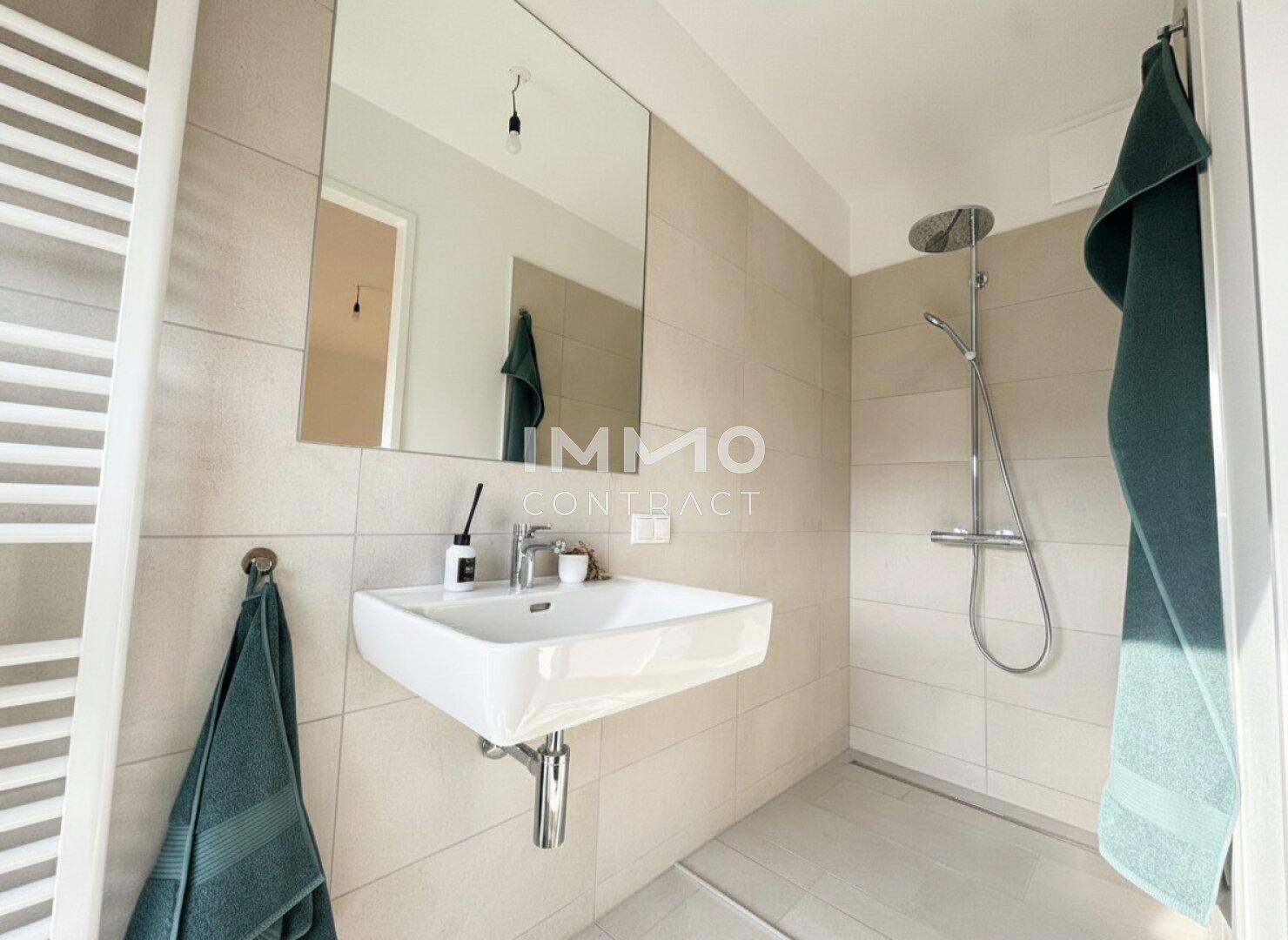 Modernes Badezimmer mit ebenerdiger Dusche, beigefarbenen Fliesen und Handtuchheizkörper.