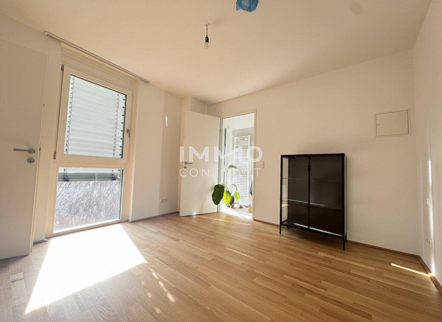 Heller Raum mit Parkettboden, großen Fenstern und Zugang zu einem Außenbereich.