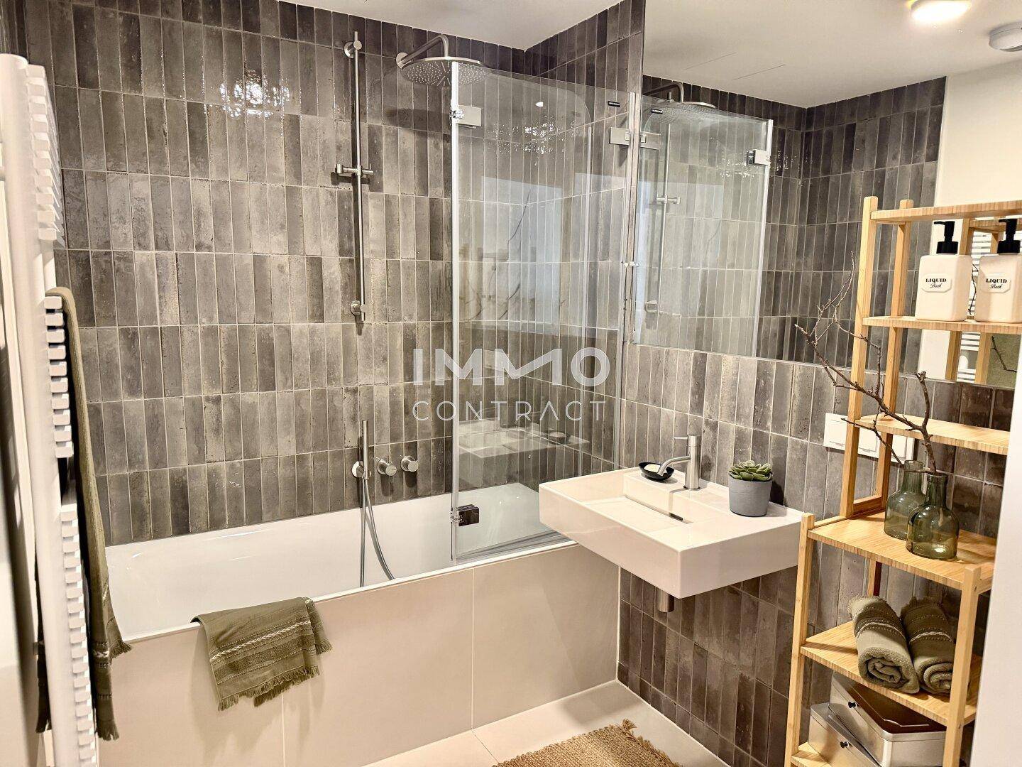 Modernes Badezimmer mit grauen Fliesen, Badewanne mit Duschabtrennung und schwebendem Waschbecken.