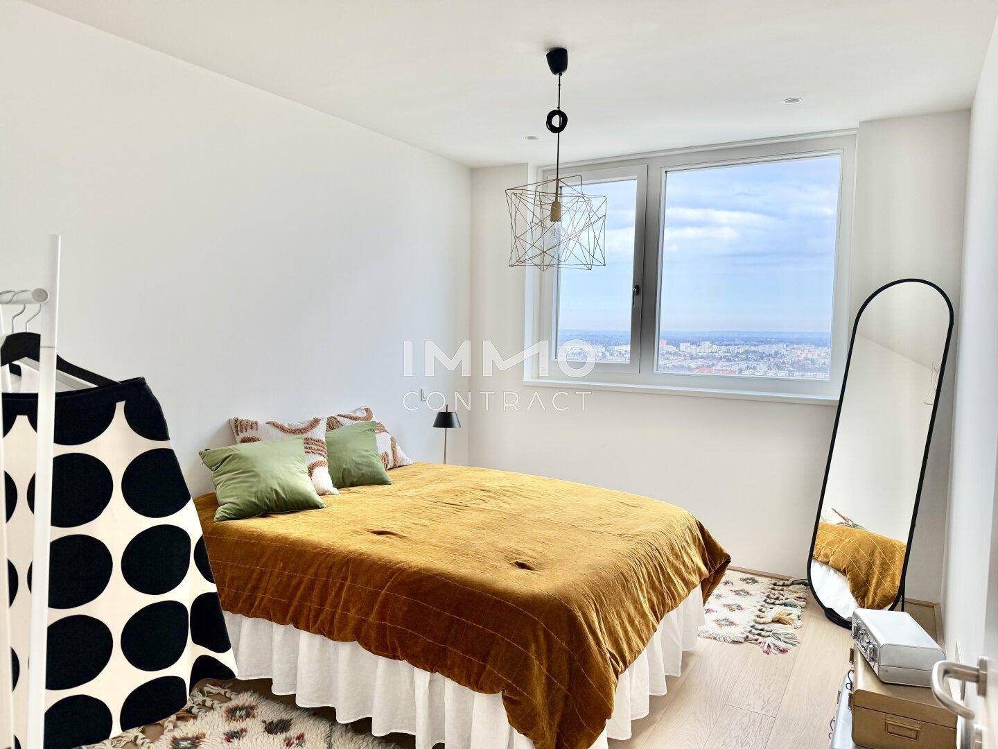 Helles Schlafzimmer mit großem Fenster, das einen weiten Blick über die Stadt bietet.