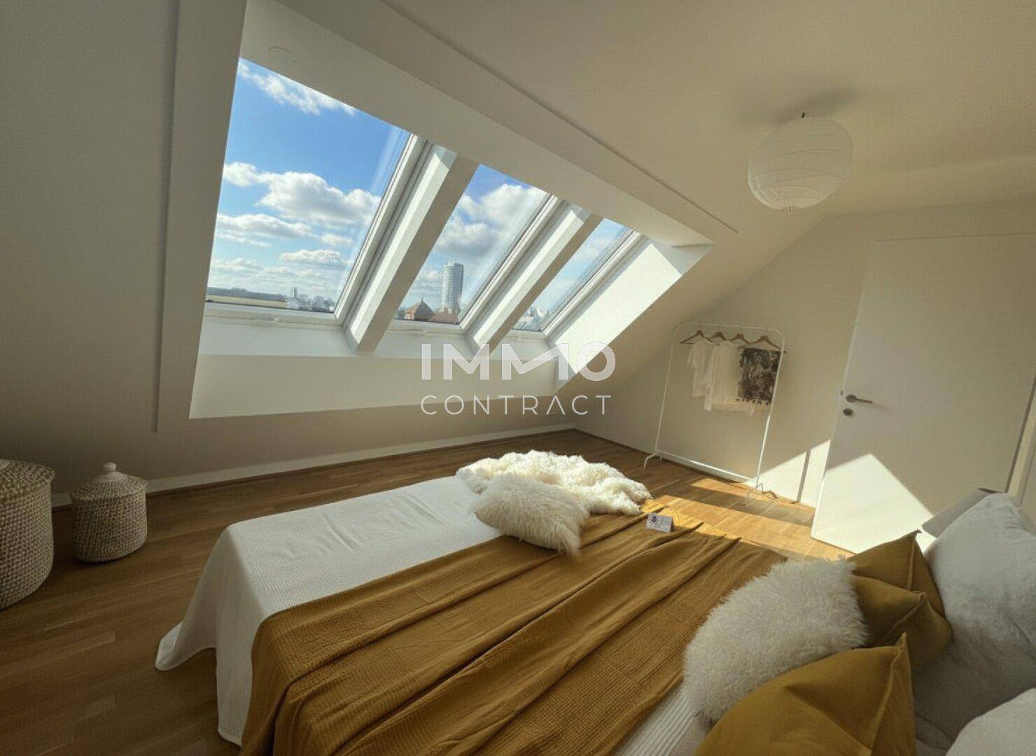Helles Schlafzimmer im Dachgeschoss mit großen Dachfenstern und Holzboden.