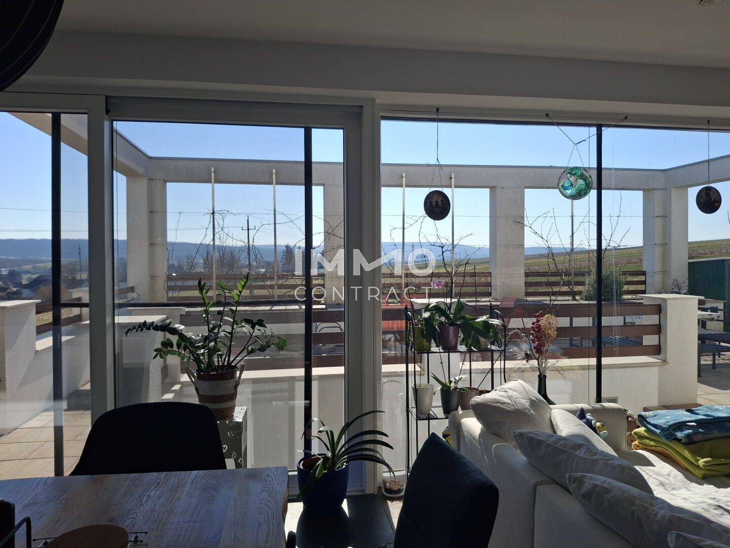Große Fensterfront im Wohnzimmer bietet weiten Blick auf die umliegende Landschaft und Terrasse.