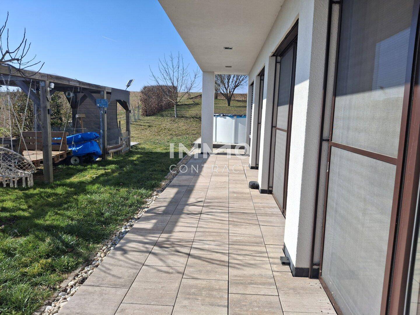 Gepflasterter Weg entlang des Hauses führt zum Gartenbereich mit Schaukel.