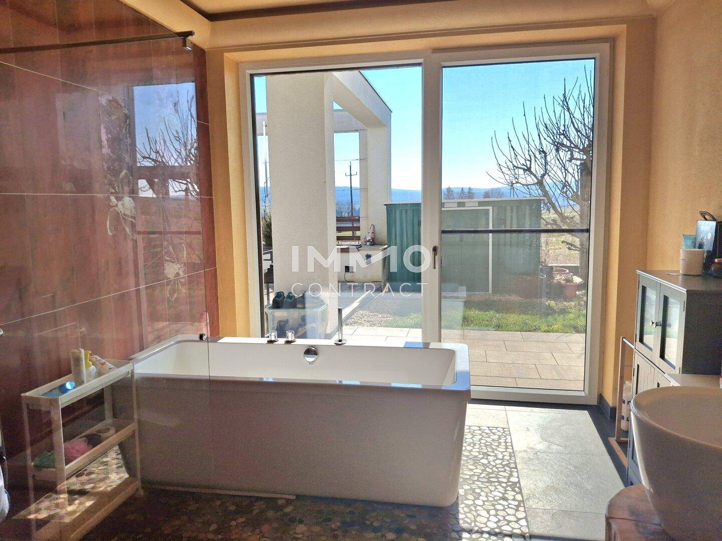 Modernes Badezimmer mit freistehender Badewanne und großen Fenstern zum Garten.