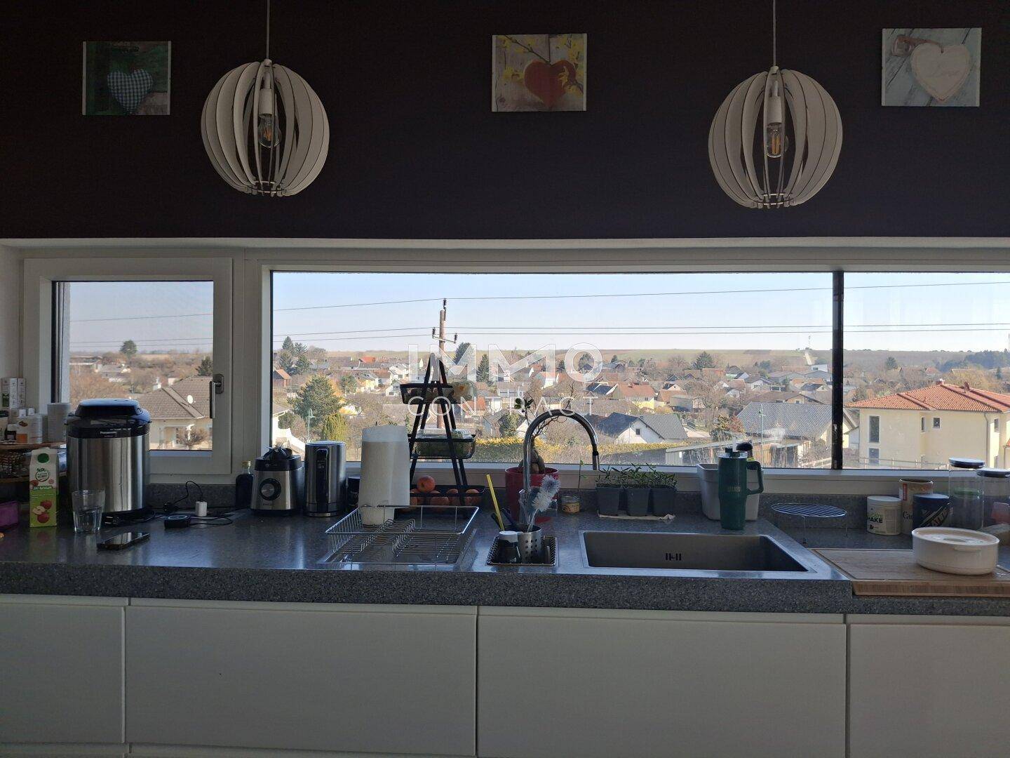 Moderne Küche mit breitem Fenster, das einen weiten Blick über die Dächer bietet.
