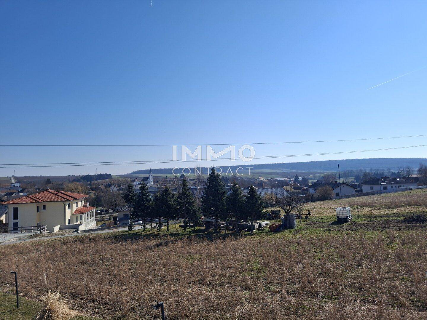Weitläufige Landschaft mit Feldern und vereinzelten Häusern unter blauem Himmel.