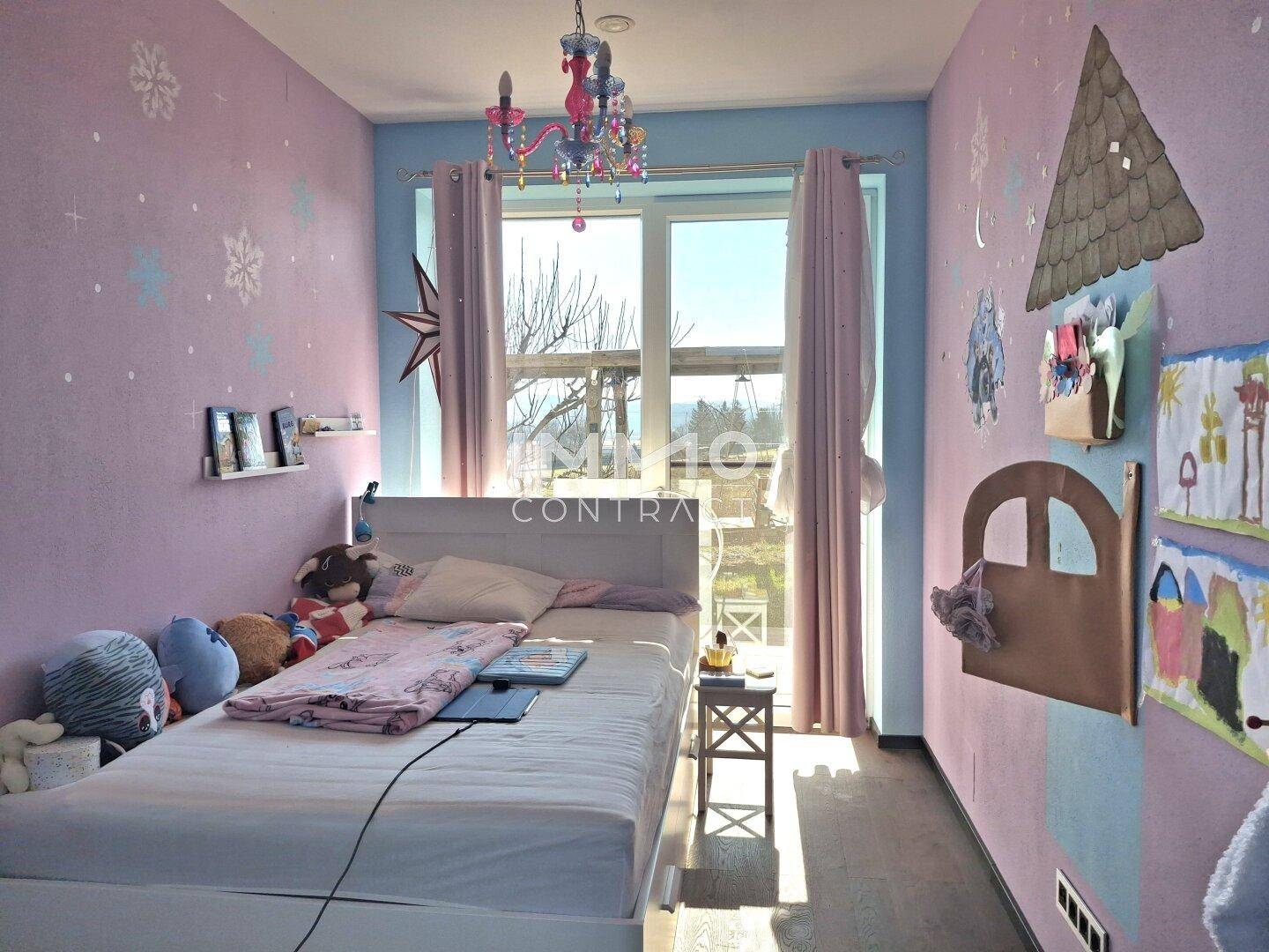 Farbenfrohes Kinderzimmer mit Einzelbett, großen Fenstern und Blick ins Grüne.