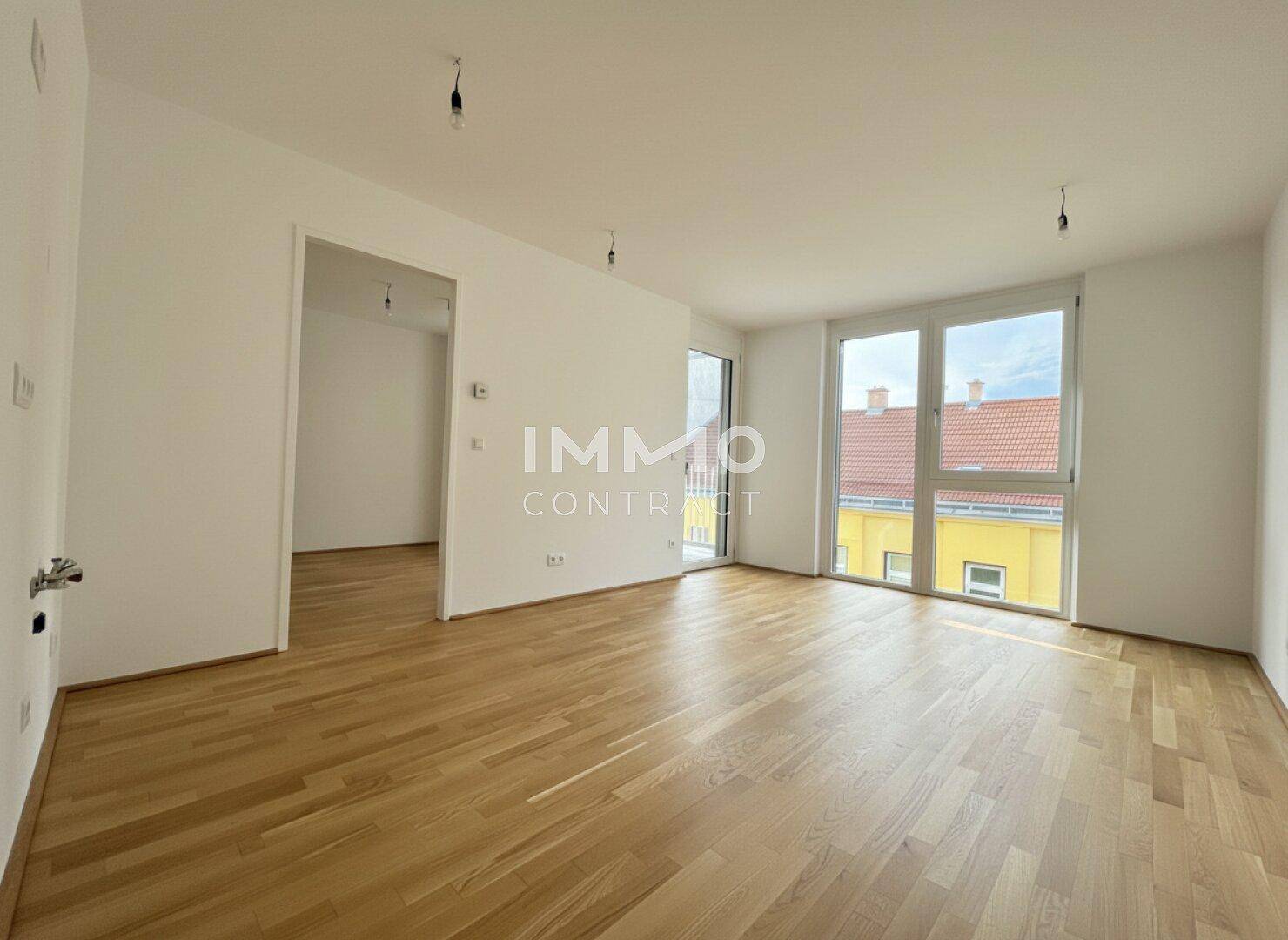 Heller, leerer Raum mit Holzboden und Zugang zu einem Balkon.