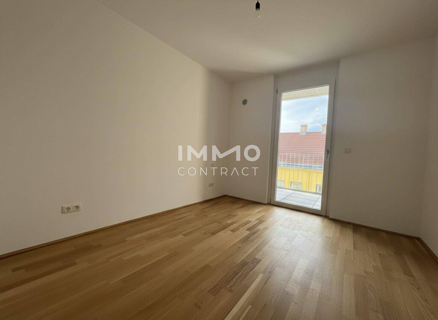 Leerer Raum mit Holzboden und großer Balkontür, bietet viel Tageslicht.