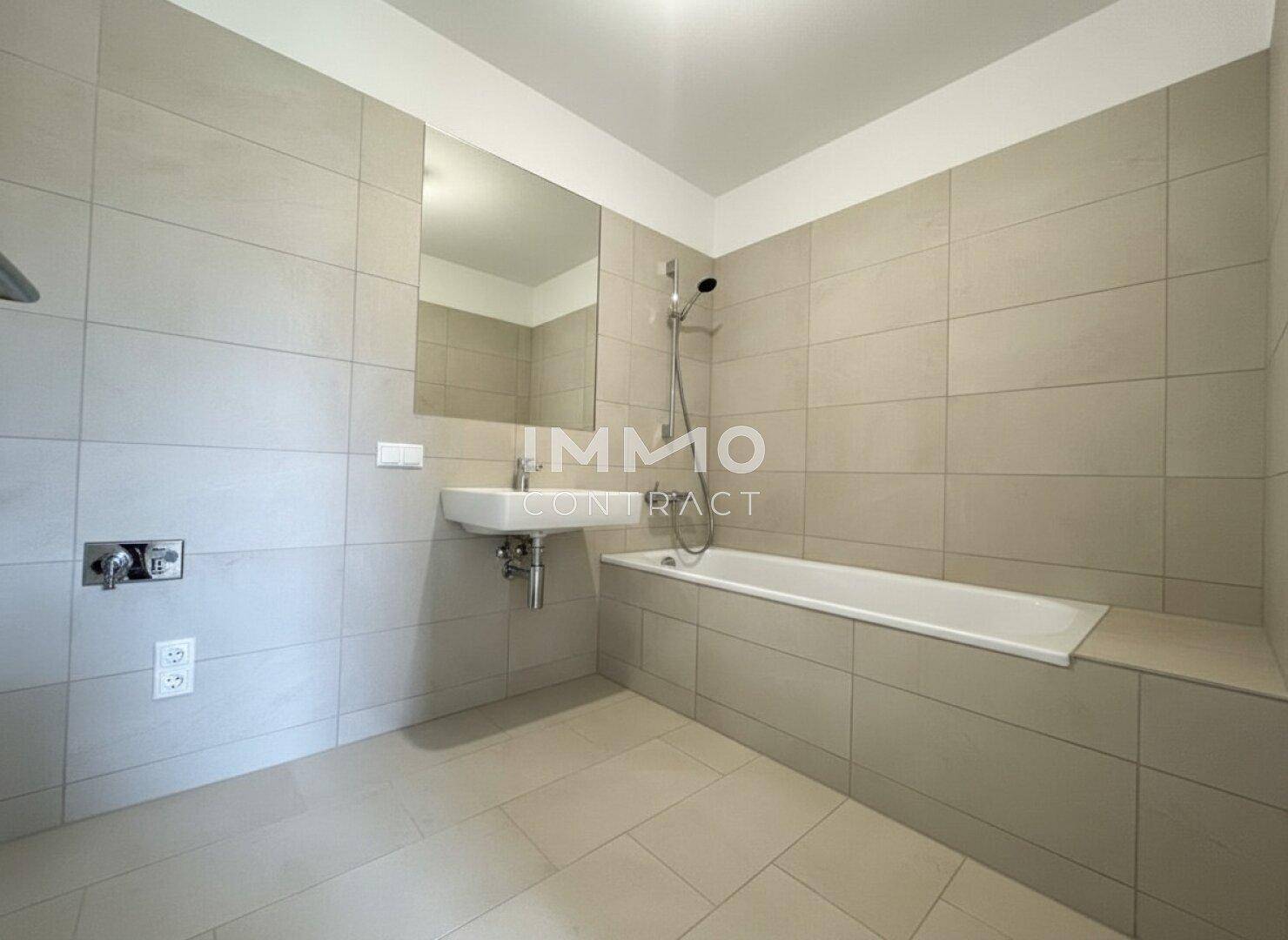 Modernes Badezimmer mit Badewanne, Waschbecken und großen hellgrauen Fliesen.