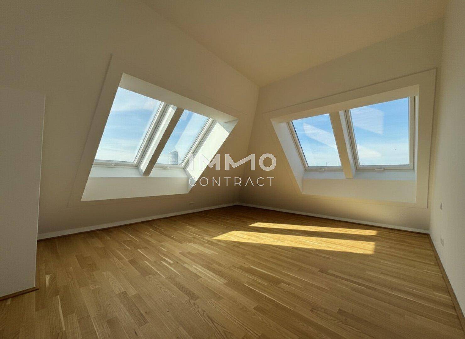 Geräumiges Schlafzimmer mit schrägen Wänden, Parkettboden und zwei großen Dachfenstern.