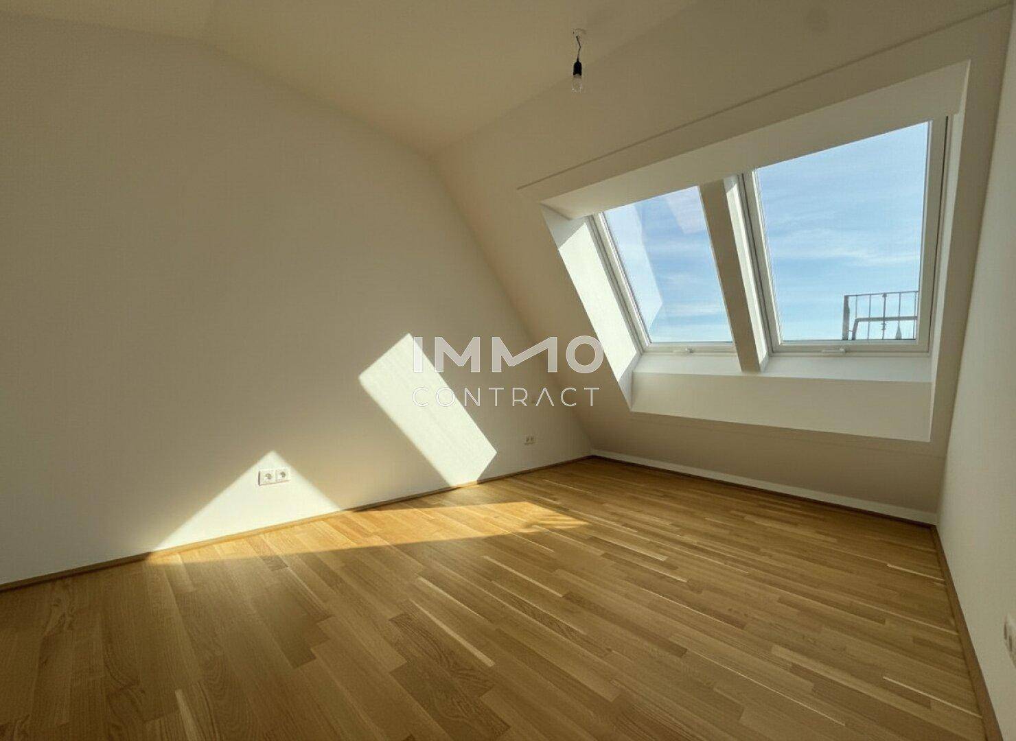 Helles Zimmer mit Holzboden und einem großen Dachfenster, das viel Sonnenlicht hereinlässt.