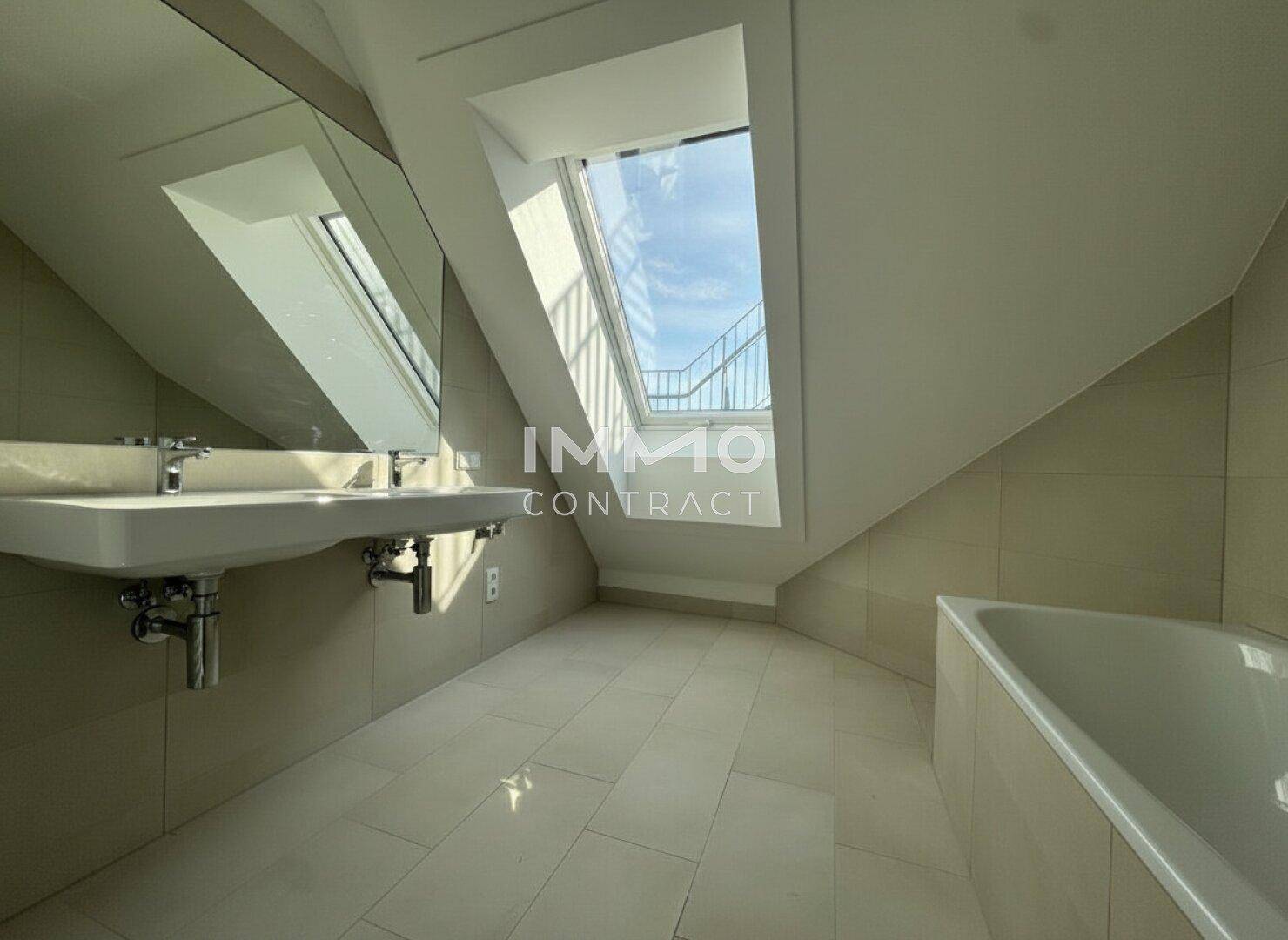 Modernes Badezimmer mit Doppelwaschbecken, Badewanne und Dachfenster für natürliches Licht.