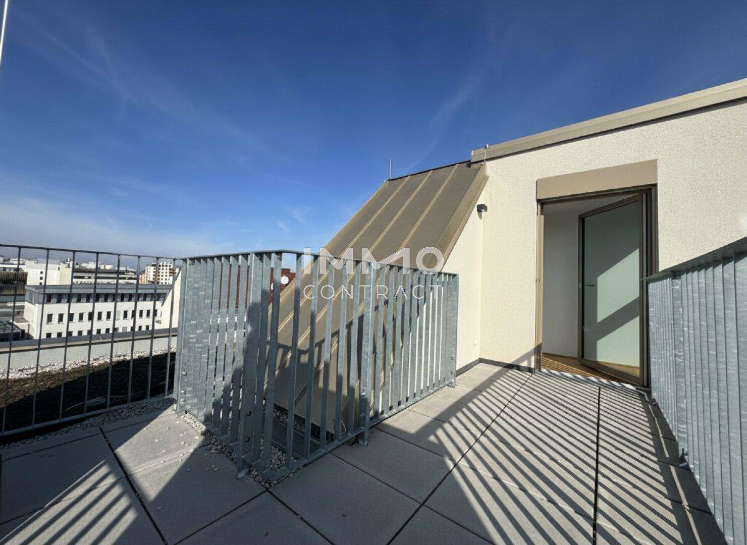 Sonniger Dachterrassenbereich mit Metallgeländer und weitem Blick über die Dächer der Stadt.
