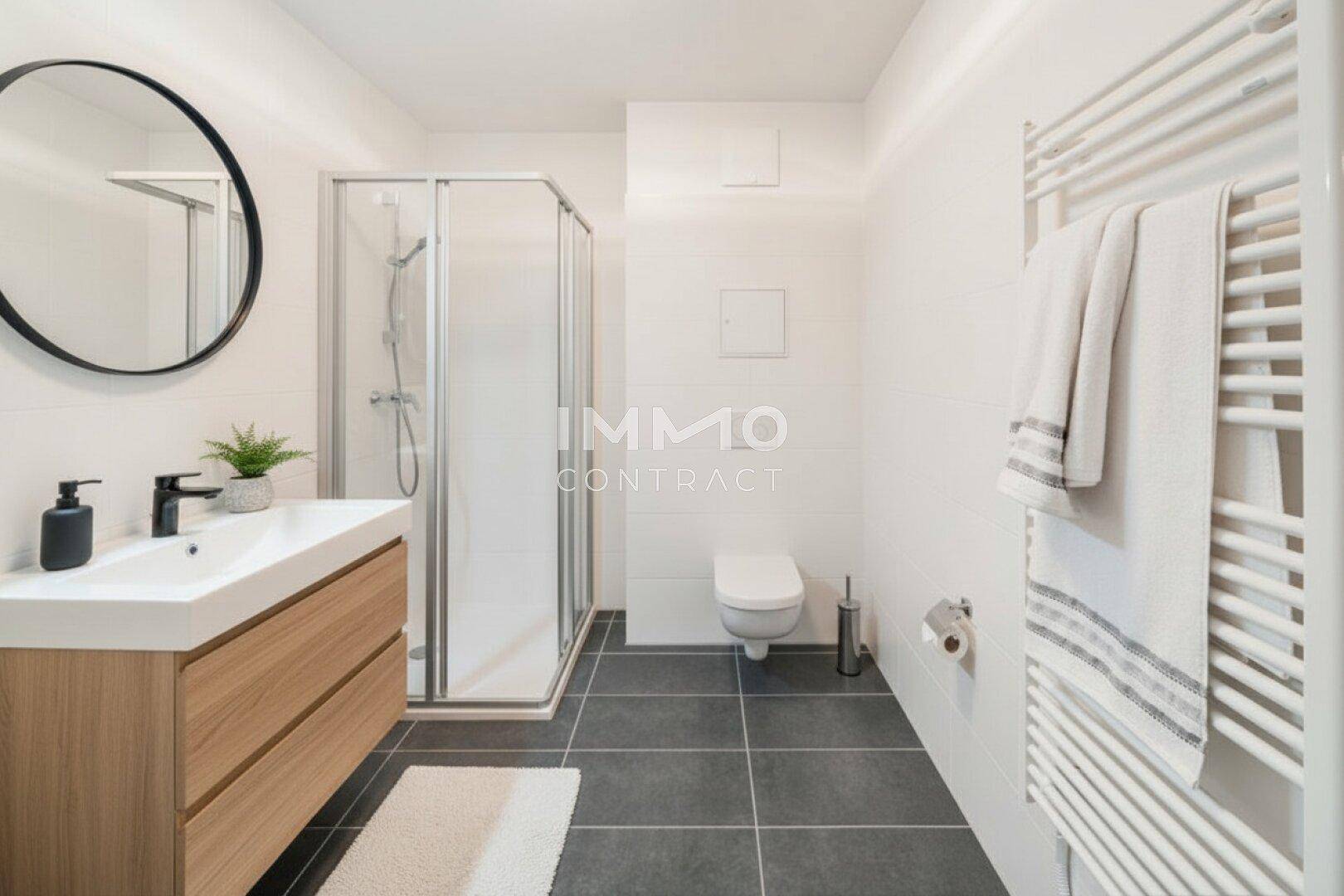 Modernes Badezimmer mit Dusche, wandhängendem WC, dunklen Fliesen und beheiztem Handtuchhalter.