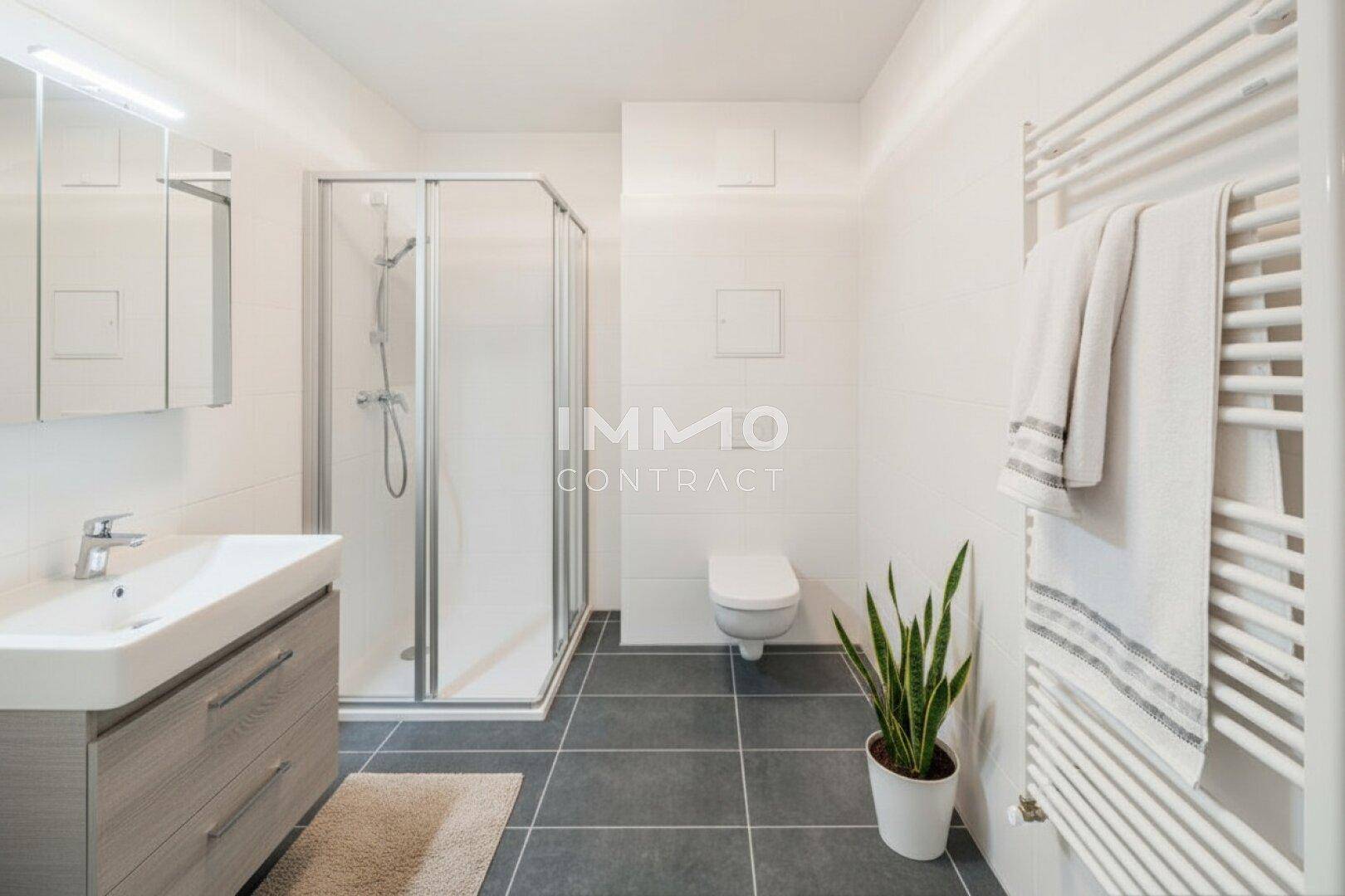 Modernes Badezimmer mit Duschkabine, Wand-WC, Waschtisch und beheiztem Handtuchhalter.